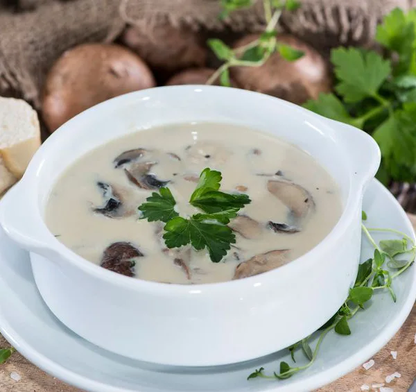 מרק פטריות קרמי עם חתיכות פטריות וברקע פטרוזיליה ופרוסות בגט
