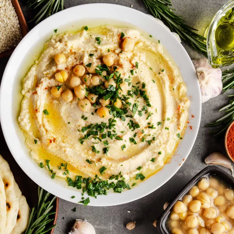 צלחת חומוס עם גרגרים ומסביב פיתות שמן זית שומשום ותבלינים