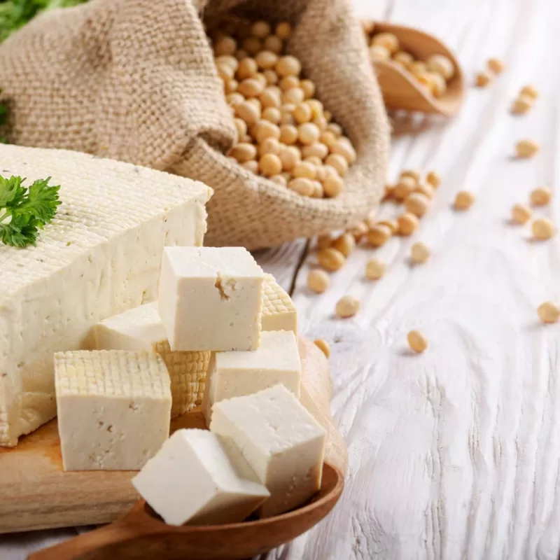 בלוק של טופו שחלקו חתוך לקוביות ומאחור פולי סויה יבשים
