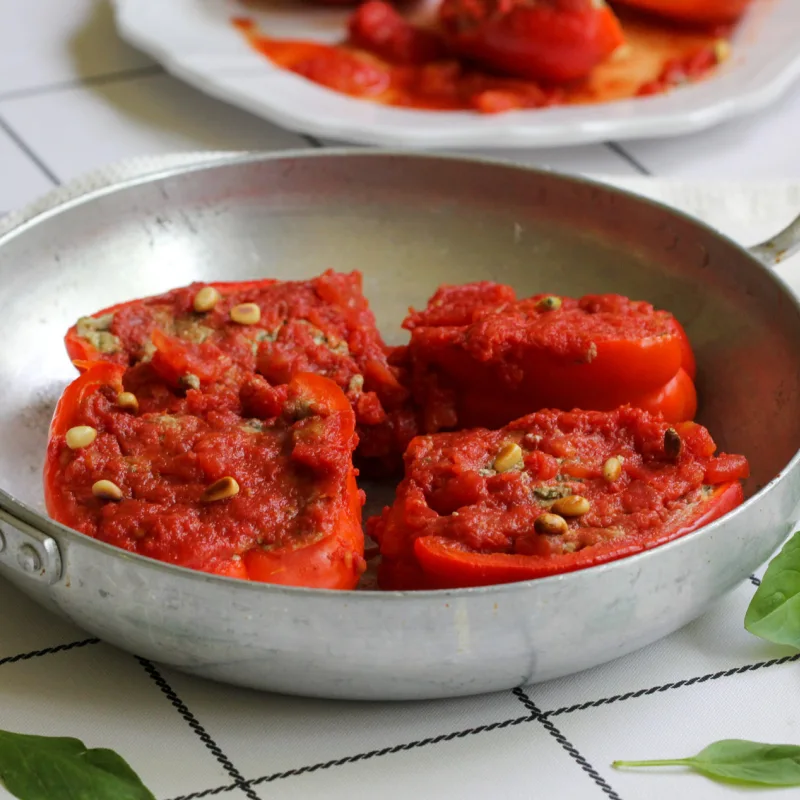 מחבת הגשה עם סירות פלפלים ממולאות בטופו עם פסטו, צנוברים ורוטב עגבניות לצד עלי בזיליקום לקישוט